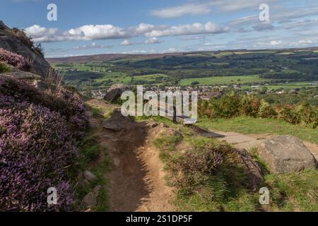 Un posto a sedere in legno accanto alle rocce di mucca e vitello su Ilkley Moor con vedute a lunga distanza sulla Wharfedale Valley. Foto Stock