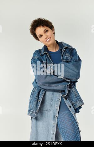 Una giovane donna elegante trasuda fiducia nei denim alla moda mentre si posa su uno sfondo neutro. Foto Stock