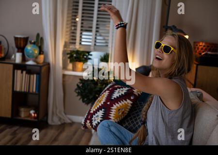 Una giovane donna gioiosa che balla a casa mentre indossa eleganti occhiali da sole e sorride Foto Stock