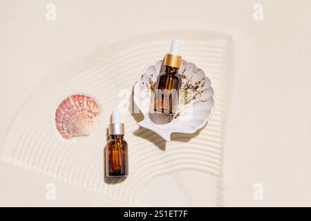 Due bottiglie cosmetiche con contagocce con un prodotto idratante e nutriente per la cura della pelle secca su sabbia marina bianca e conchiglie. vista dall'alto Foto Stock