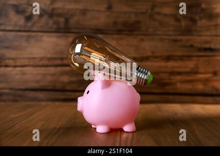 Salvadanaio e lampadina su un tavolo di legno. Concetto di risparmio energetico Foto Stock