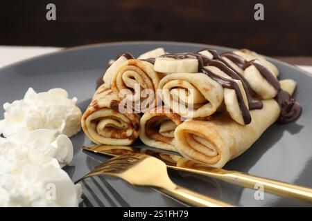 Deliziose crepe con salsa al cioccolato, banana e panna montata sul piatto, primo piano Foto Stock
