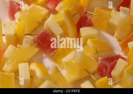 Gli spiedini di frutta fresca mostrano una varietà di pezzi gialli e rossi, perfetti per incontri estivi e spuntini salutari. Foto Stock