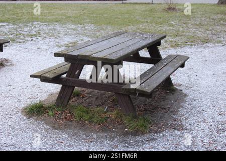 Un tavolo da picnic in legno si trova in un parco coperto da una leggera spolveratura di neve in una fredda giornata invernale. L'erba sbircia attraverso la neve intorno al tavolo. Foto Stock