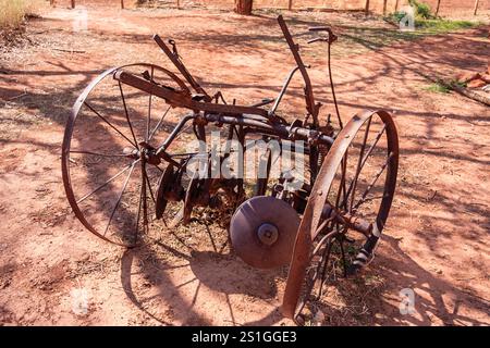 Un vecchio aratro arrugginito è seduto a terra. L'aratro è realizzato in metallo ed è dotato di una ruota grande. La scena è ambientata in un'area asciutta e polverosa, con molti dir Foto Stock