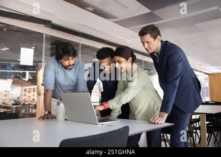 Team aziendale multietnico composto da giovani colleghi in piedi davanti a un notebook Foto Stock