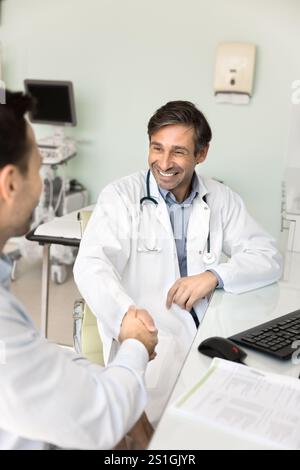 Medico ecografo della clinica felice e sicuro che stringe la mano ai colleghi Foto Stock