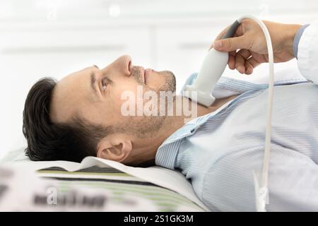 Vista laterale del paziente di sesso maschile ecografista ospite per l'esame della tiroide Foto Stock