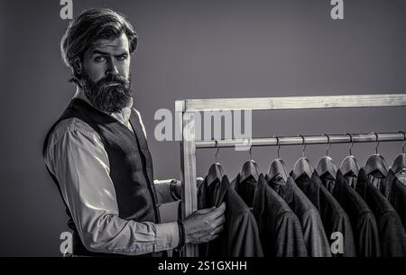 Ritratto di un giovane barbuto, in un negozio di abbigliamento maschile sceglie un abito da lavoro. L'uomo abbina il suo vestito alla moda con abiti firmati custome Foto Stock