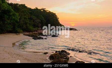 Una spiaggia tranquilla sull'isola di Koh Munnork immersa nel caldo bagliore del tramonto. Le onde si infrangono dolcemente sulla riva mentre la vegetazione lussureggiante incornicia la costa, creando una fuga perfetta per gli amanti della natura. Foto Stock