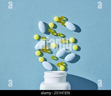 varie pillole e capsule colorate e bottiglia bianca su sfondo blu, vista dall'alto Foto Stock