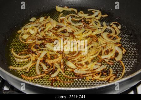 Fette di cipolla caramellate dorate saltate in padella a fuoco medio, brillando con olio d'oliva. Perfetto per esaltare i sapori dei piatti. Il Foto Stock