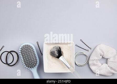Vista piatta dello shampoo in polvere secco fatto in casa in un recipiente bianco, con pennello per trucco applicato su sfondo grigio. Concetto di cura dei capelli senza sprechi. Foto Stock
