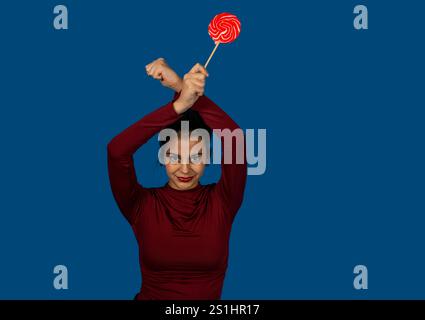 Ritratto in studio di una giovane donna con un lecca-lecca, isolato su sfondo blu Foto Stock