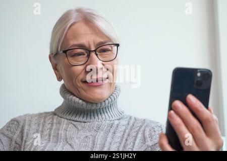 Donna anziana che si diverte a fare acquisti online utilizzando il suo smartphone Foto Stock