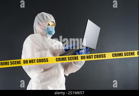 L'analisi legale con laptop in abbigliamento protettivo funziona sulla scena del crimine. Il concetto di risolvere un crimine. Vero crimine. Foto Stock