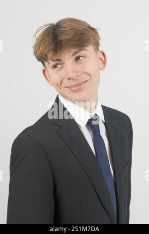 Felice ragazzo di sedici anni che indossa un completo, girato in studio su sfondo bianco Foto Stock