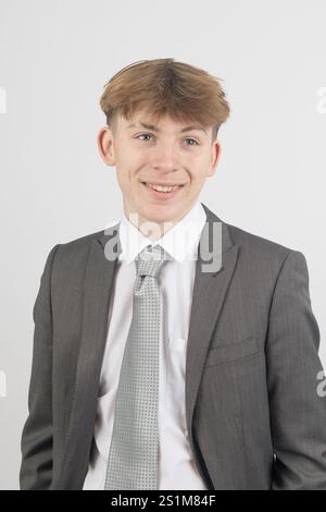 Felice ragazzo di sedici anni che indossa un completo, girato in studio su sfondo bianco Foto Stock