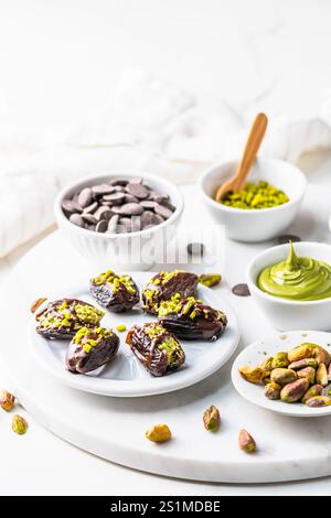 Datteri pieni di croccante crema al pistacchio e ricoperti di cioccolato, datteri al cioccolato di Dubai, sfondo bianco. Organizzato con ingredienti. Verticale con Foto Stock