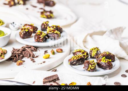 Datteri pieni di croccante crema al pistacchio e ricoperti di cioccolato, datteri al cioccolato di Dubai, sfondo bianco. Organizzato con ingredienti. Foto Stock