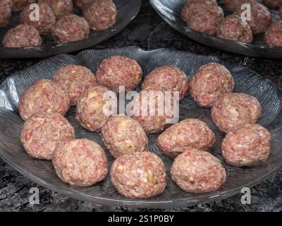 Le tradizionali polpette svedesi, crude e preparate con cura, si siedono su un piatto di vetro, pronte per essere fritte e trasformate in un classico piatto nordico. Foto Stock