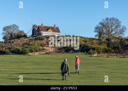 Gli escursionisti si avvicinano al mulino a vento di Reigate Heath accanto al circolo del Reigate Heath Golf Club, Surrey, Inghilterra, Regno Unito, in una soleggiata giornata invernale con cielo azzurro Foto Stock