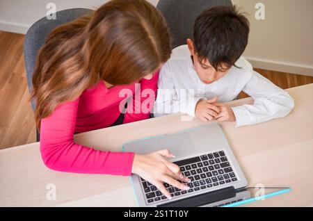 Madre che assiste il bambino con la scuola a casa, utilizzando un notebook per l'istruzione online e le attività di elearning Foto Stock