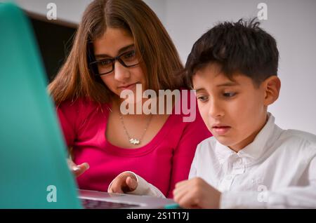 Adolescente che aiuta il fratello minore a studiare e fare i compiti utilizzando un computer portatile Foto Stock