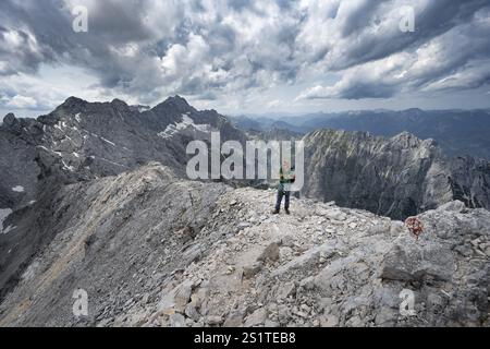 Alpinista con casco su uno stretto sentiero roccioso, attraversando il Jubilaeumsgrat, vista di Zugspitze e Hoellental in ripido paesaggio roccioso di montagna, ascen Foto Stock