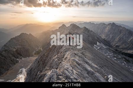 Alpinista con casco su una stretta cresta rocciosa all'alba, attraversando il Jubilaeumsgrat, vista di Hoellental con Hoellentalferner e Alpspitze, Wette Foto Stock