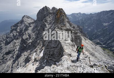 Alpinista con casco che sale in una salita sicura sulla roccia, su una stretta cresta rocciosa, attraversando il Jubilaeumsgrat, vista del Rheintal e dell'Alpspitze Foto Stock