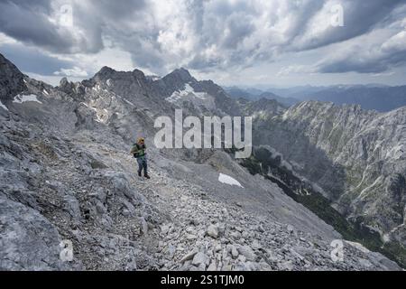 Alpinista con casco su uno stretto sentiero roccioso, attraversando il Jubilaeumsgrat, vista di Zugspitze e Hoellental in ripido paesaggio roccioso di montagna, ascen Foto Stock