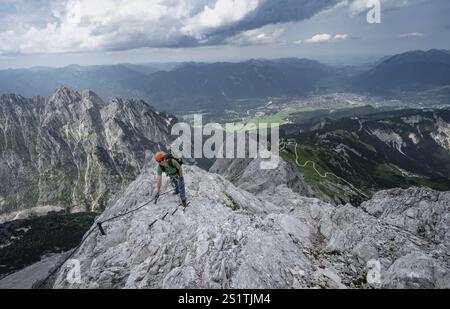 Alpinista con casco che sale sulla roccia in una salita sicura, su una stretta cresta rocciosa, in ripido paesaggio roccioso di montagna, vista di Garmisch Partenki Foto Stock