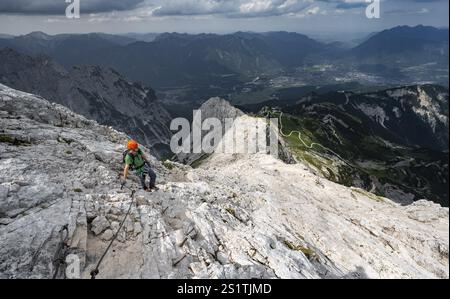 Alpinista con casco che sale sulla roccia in una salita sicura, su una stretta cresta rocciosa, in ripido paesaggio roccioso di montagna, vista di Garmisch Partenki Foto Stock