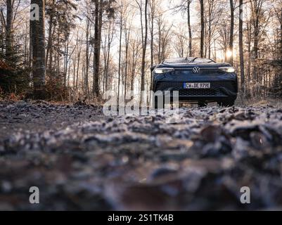 Un'auto dalla parte anteriore su un sentiero boschivo ghiacciato all'alba, car sharing, auto elettrica, Volkswagen ID 5, Gechingen, regione di Hecken und Gaeu, Foresta Nera, Foto Stock