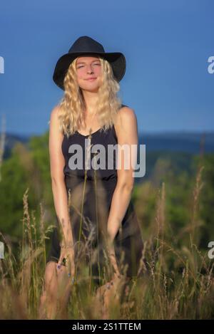 Ritratti la giovane donna bionda in mezzo alla natura in una serata estiva. Giovane donna con lunghi capelli biondi nella natura estiva Foto Stock