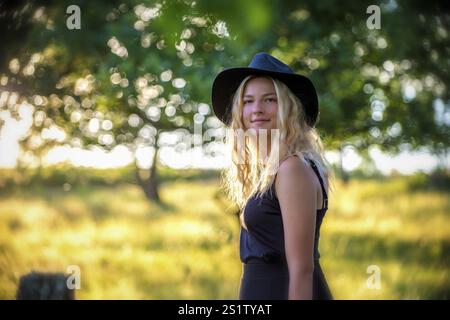 Ritratti la giovane donna bionda in mezzo alla natura in una serata estiva. Giovane donna con lunghi capelli biondi nella natura estiva Foto Stock