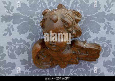 Angelo di legno intagliato su carta da parati grigia Foto Stock