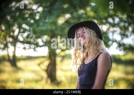 Ritratti la giovane donna bionda in mezzo alla natura in una serata estiva. Giovane donna con lunghi capelli biondi nella natura estiva Foto Stock