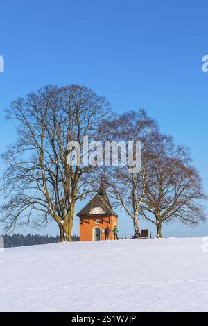 La piccola cappella rossa di Friesenhagen in un paesaggio invernale innevato e soleggiato. Cappella rossa in inverno con paesaggio innevato e sole Foto Stock