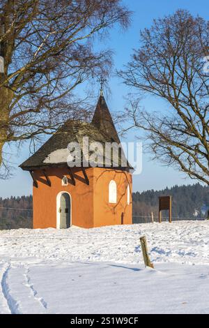 La piccola cappella rossa di Friesenhagen in un paesaggio invernale innevato e soleggiato. Cappella rossa in inverno con paesaggio innevato e sole Foto Stock