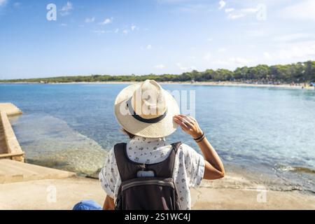 Turista con zaino e cappello di paglia che si gode la giornata di sole sulla spiaggia di estanys a colonia de sant jordi, maiorca, isole baleari, spagna Foto Stock