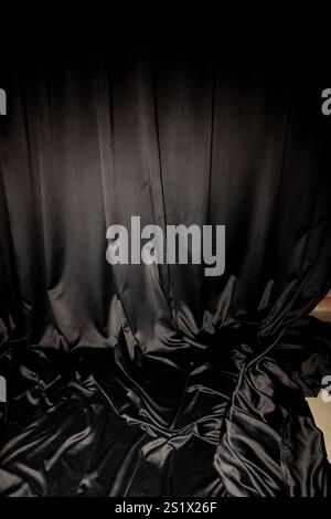 Tessuto nero lucido o tenda avvolto su pareti e pavimento in uno studio fotografico o a casa, che funge da sfondo. Foto di alta qualità Foto Stock
