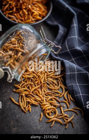 Vermi salati secchi. Vermi arrostiti in vasetto su un tavolo nero. Foto Stock