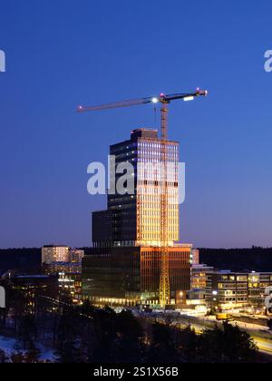 Moderno edificio grattacielo con facciata in vetro con una gru sullo sfondo del cielo limpido, che costruisce l'edificio degli uffici di Sickla Central Foto Stock