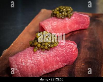 Due deliziosi nigiri di tonno conditi con scintillante caviale verde, serviti su una tavola rustica di legno, per creare un'esperienza culinaria sofisticata Foto Stock