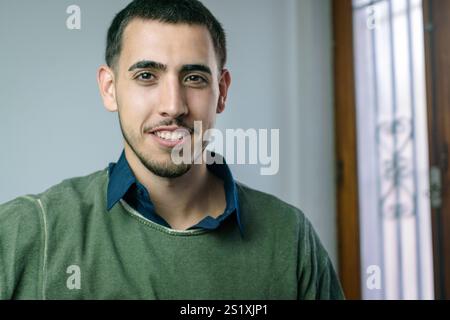 Ritratto interno di un giovane sorridente che indossa un maglione verde e una camicia blu Foto Stock