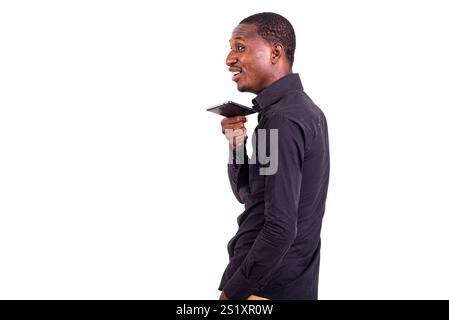 giovane uomo d'affari in camicia nera in piedi su sfondo bianco che parla sorridendo al cellulare. Foto Stock