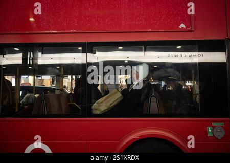 Donna che naviga sullo smartphone mentre viaggia su un autobus di Londra con foulard hijab, Oxford Street, Londra, Inghilterra, Regno Unito Foto Stock