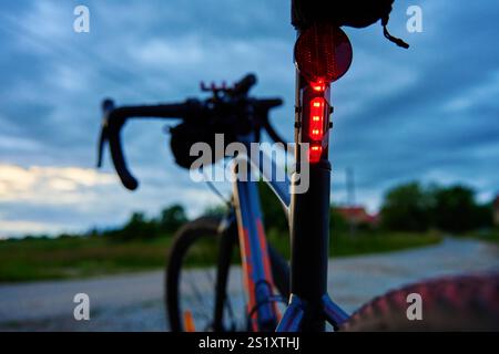 Luce di posizione posteriore per biciclette illuminata al crepuscolo. Luce di arresto rossa per la visibilità e la sicurezza del ciclista durante il ciclismo notturno. Luce posteriore a LED sulla moto Foto Stock